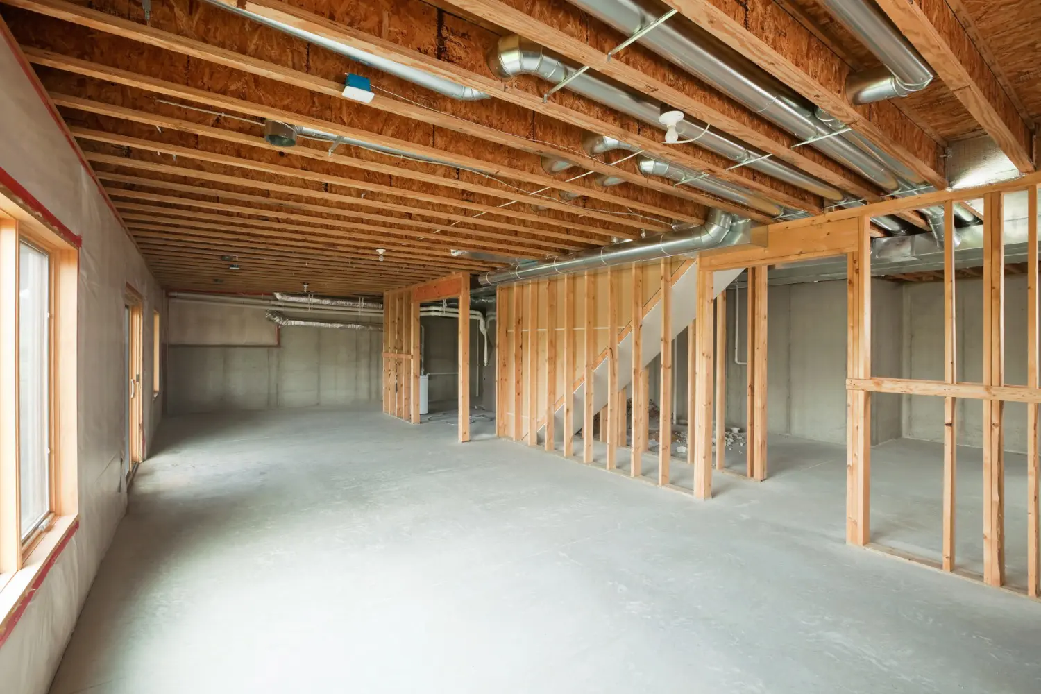 Unfinished basement with exposed wooden beams, ductwork, and unpainted walls. Concrete floor and framed wooden partitions are visible, along with some windows.