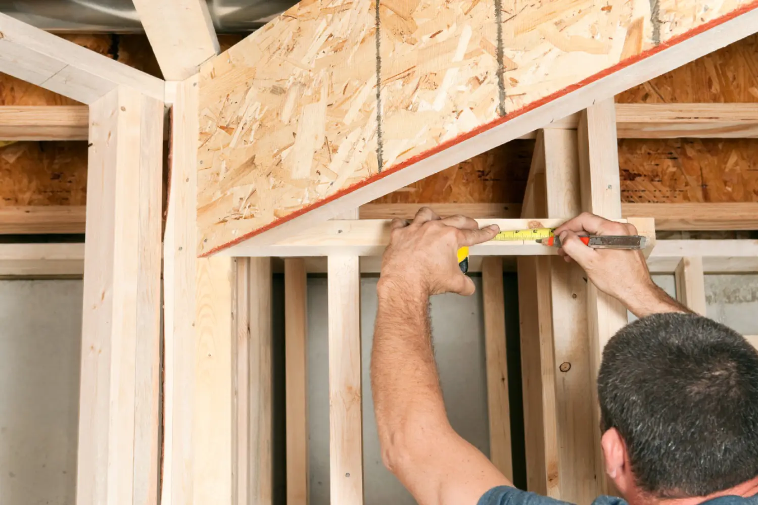 Person measuring wooden beams with a tape measure in a building under construction.