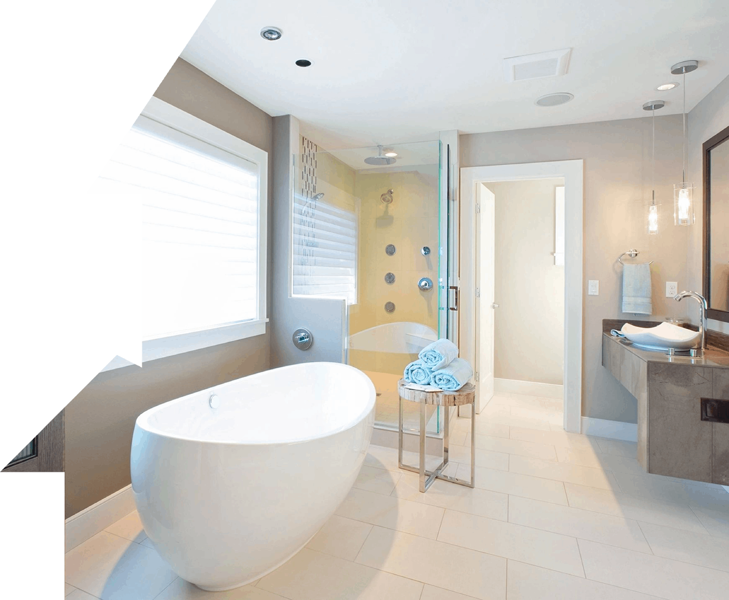 Modern bathroom with a freestanding tub, glass-enclosed shower, white tiles, and a sink on a wooden counter. Rolled towels are placed on a stand beside the tub.